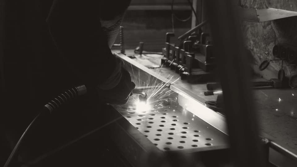 A worker welding a piece of metal in a factory, representing the industrial manufacturing context glass fibre products are used in.