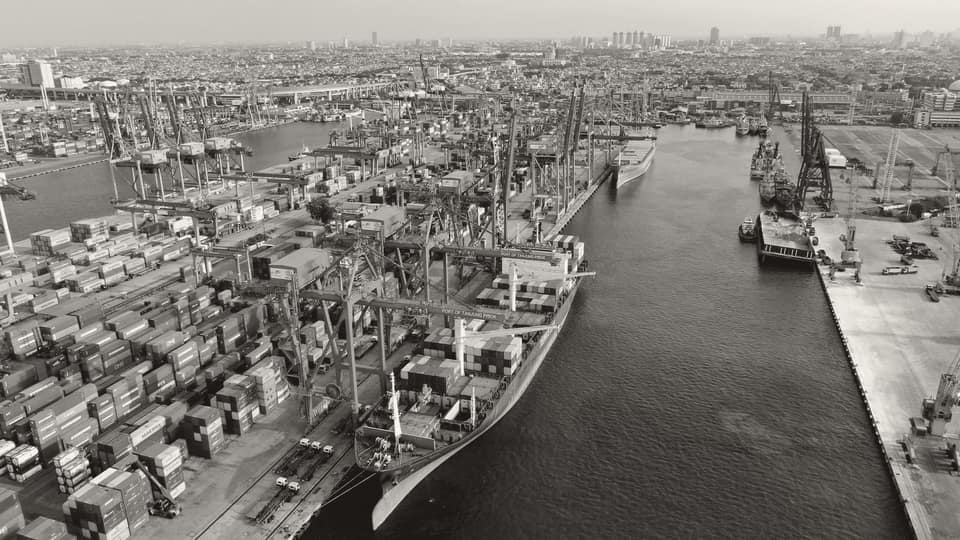 A busy shipping port with cranes and stacked cargo containers, the entry point for imported soda ash.