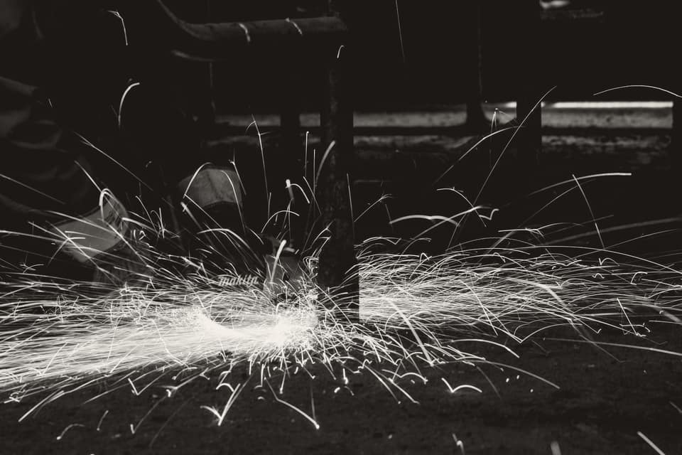 A metalworker cutting steel with an angle grinder, sparks flying, in an industrial fabrication shop. Anti-dumping cases most often concern basic metals and industrial inputs like this.