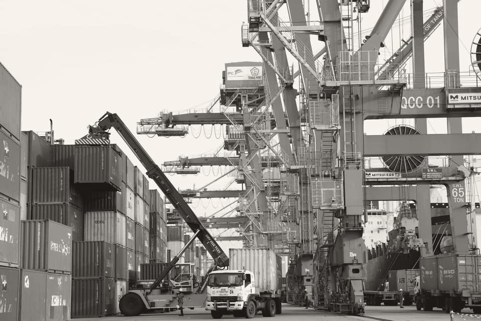 A container ship being loaded by gantry cranes and a forklift at a shipping terminal, the kind of trade infrastructure a DGTR investigation ultimately reaches into.
